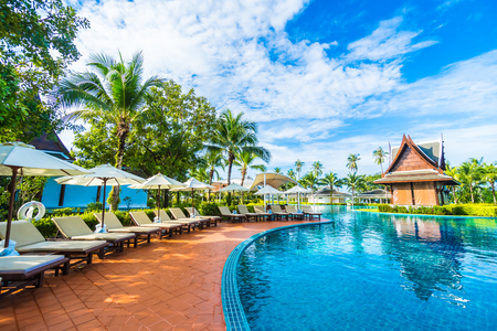 Beautiful luxury umbrella and chair around outdoor swimming pool in hotel and resort with coconut palm tree on blue sky - Boost up color Processingの写真素材