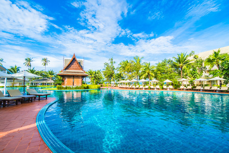 Beautiful luxury umbrella and chair around outdoor swimming pool in hotel and resort with coconut palm tree on blue sky - Boost up color Processingの写真素材