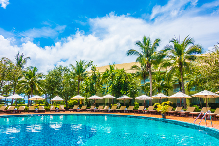 Beautiful luxury umbrella and chair around outdoor swimming pool in hotel and resort with coconut palm tree on blue sky - Boost up color Processingの写真素材