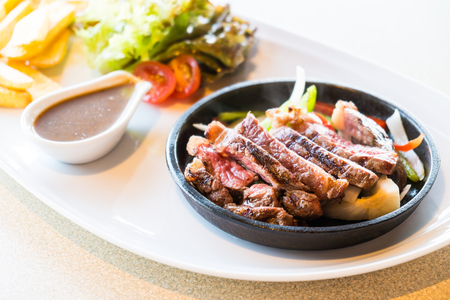 Selective focus point on Steak beef meat in hot pan with french fries and vegetableの写真素材