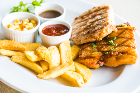 Pork chop and Chicken steak with french fries and sauce in white plateの写真素材