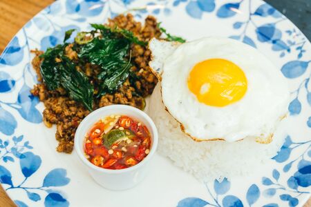 Spicy pork with basil leaf and rice on top with fried eggs in plate - Thai food styleの写真素材