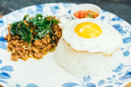 Spicy pork with basil leaf and rice on top with fried eggs in plate - Thai food style