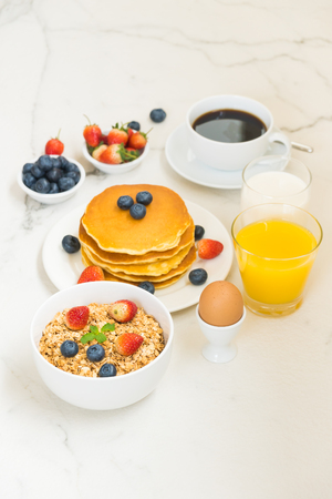 Healthy Breakfast set with Pancake and Granola with blueberry and strawberry and black coffee , Milk and Orange juice on white stone table backgroundの写真素材