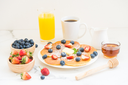 Healthy Breakfast set with Pancake blueberry and strawberry fruits and black coffee , Milk and Orange juice on white stone table backgroundの写真素材