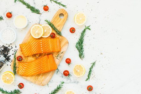 Raw and fresh salmon meat fillet on wooden cutting board with lemon tomato and other ingredient - Healthy food styleの写真素材