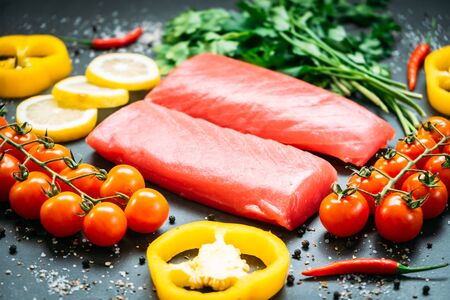 Raw tuna fish fillet meat on wooden cutting board with vegetable and ingredient for cooking on black stone backgroundの写真素材