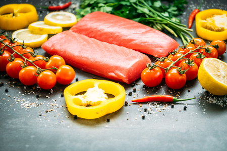 Raw tuna fish fillet meat on wooden cutting board with vegetable and ingredient for cooking on black stone backgroundの写真素材