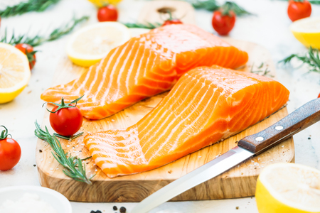 Raw and fresh salmon meat fillet on wooden cutting board with lemon tomato and other ingredient - Healthy food styleの写真素材