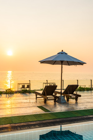 Beautiful umbrella and chair around swimming pool in hotel and resort in sunrise timeの写真素材