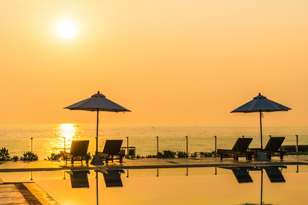Beautiful umbrella and chair around swimming pool in hotel and resort in sunrise timeの写真素材
