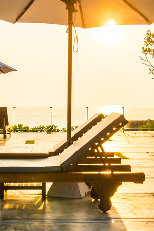 Beautiful umbrella and chair around swimming pool in hotel and resort in sunrise timeの写真素材