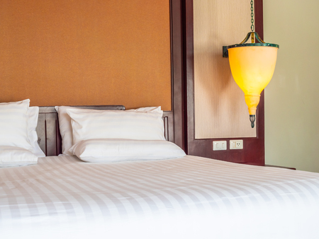 Comfortable pillow on bed with light lamp decoration in hotel bedroomの写真素材
