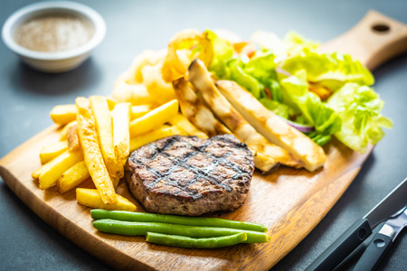 Grilled beef meat steak with french fries sauce and fresh vegetable on wooden cutting boardの写真素材