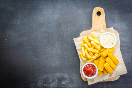 Fish finger and french fries or chips with tomato ketchup and mayonnaise sauce on wooden cutting board - Unhealthy food styleの写真素材