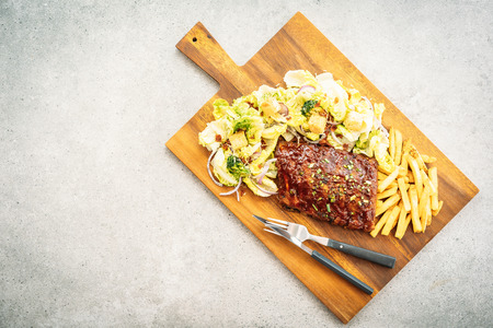 Grilled bbq pork rips with french fries and vegetable on wooden plateの写真素材