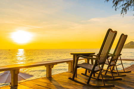 Empty wood chair and table at outdoor patio with beautiful tropical beach and sea at sunrise or sunset background for vacation and travelの写真素材