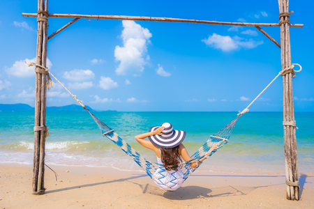 Portrait beautiful young asian woman happy smile leisure on hammock swing around the beach sea and ocean with blue sky white cloud for vacation travelの写真素材