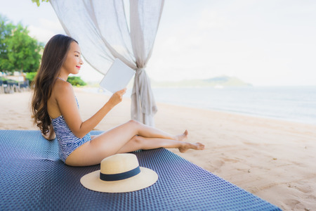 Portrait beautiful young asian woman reading book with happy smile relax in lounge bed chair on the beach sea ocean for leisure travel in vacationの写真素材