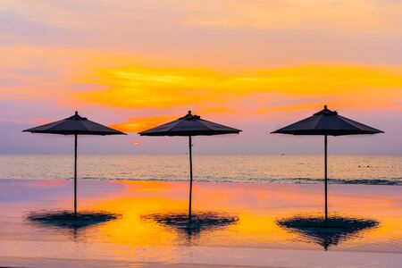 Umbrella and chair around swimming pool neary sea ocean beach at sunrise or sunset time for leisure travel and vacationの写真素材