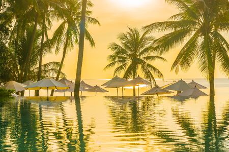 Beautiful outdoor tropical nature landscape of swimming pool in hotel resort with coconut palm tree umbrella and chair nearly sea ocean beach at sunrise timeの写真素材