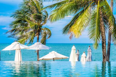 Beautiful luxury outdoor swimming pool in hotel resort with umbrella and chair and coconut palm treeの写真素材