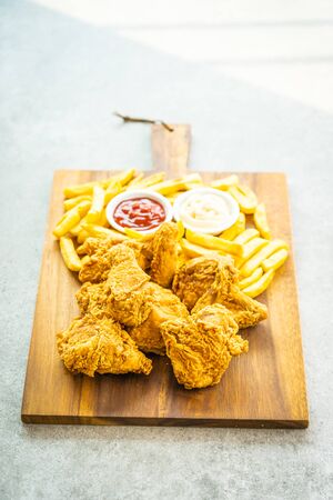 Fried chicken wings with french fries and tomato or ketchup and mayonnaise sauce on wood cutting board - Junk or Unhealthy food styleの写真素材