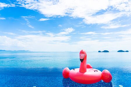 Beautiful outdoor swimming pool in hotel resort with flamingo float around sea ocean white cloud on blue sky for holiday vacation travel conceptの写真素材