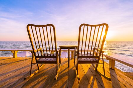 Empty wood chair and table at outdoor patio with beautiful tropical beach and sea at sunrise or sunset background for vacation and travelの写真素材