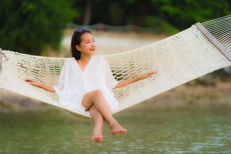 Portrait beautiful young asian woman sitting on hammock around sea beach ocean for relax in holiday vacation travel conceptの写真素材