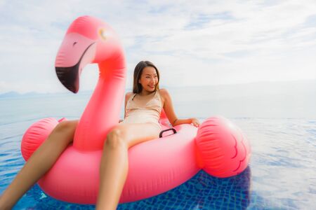 Portrait young asian woman on inflatable float flamingo around outdoor swimming pool in hotel resort...