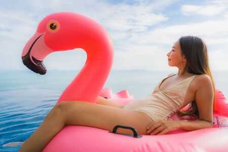 Portrait young asian woman on inflatable float flamingo around outdoor swimming pool in hotel resort for holiday vacation conceptの写真素材