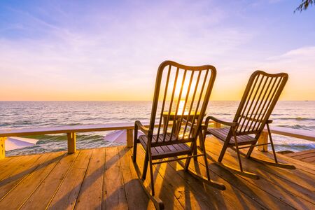 Empty wood chair and table at outdoor patio with beautiful tropical beach and sea at sunrise or sunset background for vacation and travelの写真素材