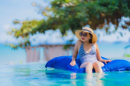 Portrait beautiful young asian woman happy smile relax in swimming pool at hotel resort neary sea ocean beach on blue sky for leisure travel in vacationの写真素材