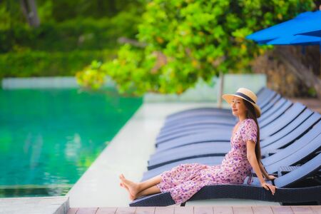 Portrait beautiful young asian woman happy smile relax in swimming pool at hotel resort nearly sea ocean beach on blue sky for leisure travel in vacationの写真素材