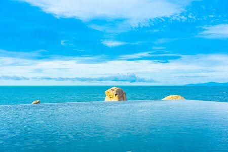 Beautiful outdoor infinity swimming pool in hotel resort with sea ocean view and white cloud blue...