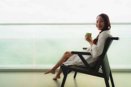 Beautiful Portrait young asian women holding coffee cup at outdoor balcony with sea ocean view for relaxの写真素材