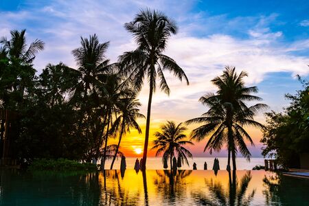 Beautiful outdoor tropical nature landscape of swimming pool in hotel resort with coconut palm tree umbrella and chair nearly sea ocean beach at sunrise timeの写真素材