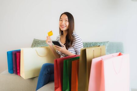 Portrait beautiful young asian women with credit card mobile phone or computer for online shopping on sofa in living room interiorの写真素材