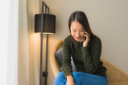 Portrait beautiful young asian women using talking mobile phone and sitting on sofa chair in living room areaの写真素材