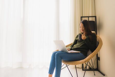 Portrait beautiful young asian women using computer or laptop for working and sitting on sofa chair in living room areaの写真素材