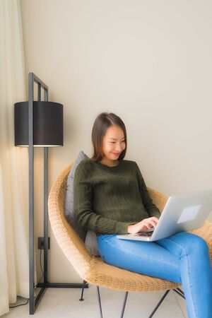 Portrait beautiful young asian women using computer or laptop for working and sitting on sofa chair in living room areaの写真素材