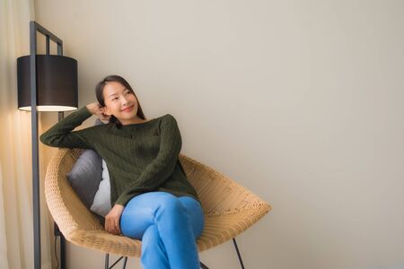 Portrait beautiful young asian women happy smile relax sitting on sofa chair in living room interiorの写真素材