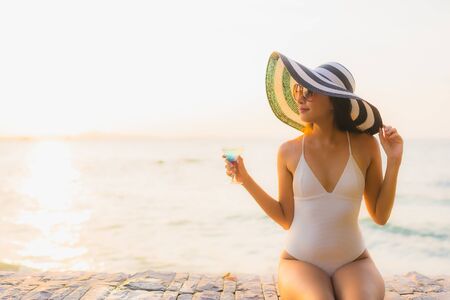 Portrait beautiful young asian women happy smile relax with cocktails glass around outdoor swimming pool in hotel resort for travel vacation at sunset or sunrise timeの写真素材
