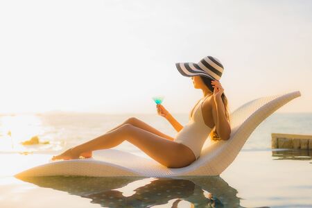 Portrait beautiful young asian women happy smile relax with cocktails glass around outdoor swimming pool in hotel resort for travel vacation at sunset or sunrise timeの写真素材