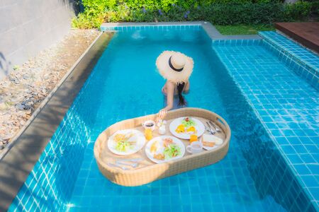 Portrait young asian woman happy smile enjoy with floating breakfast tray in swimming pool in hotel resortの写真素材