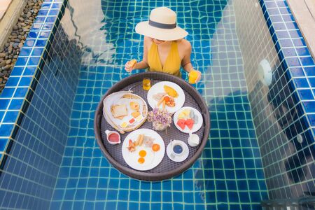 Portrait beautiful young asian woman happy smile relax with breakfast floating around swimming pool in hotel resortの写真素材