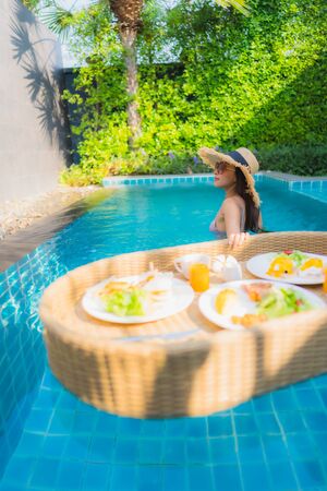 Portrait young asian woman happy smile enjoy with floating breakfast tray in swimming pool in hotel resortの写真素材