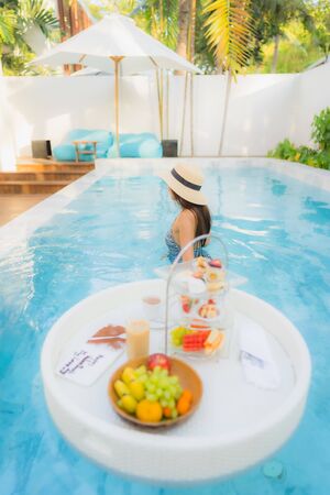 Portrait beautiful young asian woman enjoy with afternoon tea or breakfast floating on swimming pool...