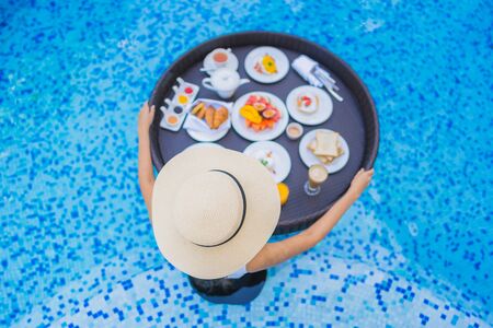 Portrait beautiful young asian woman happy smile with floating breakfast in tray on swimming poolの写真素材
